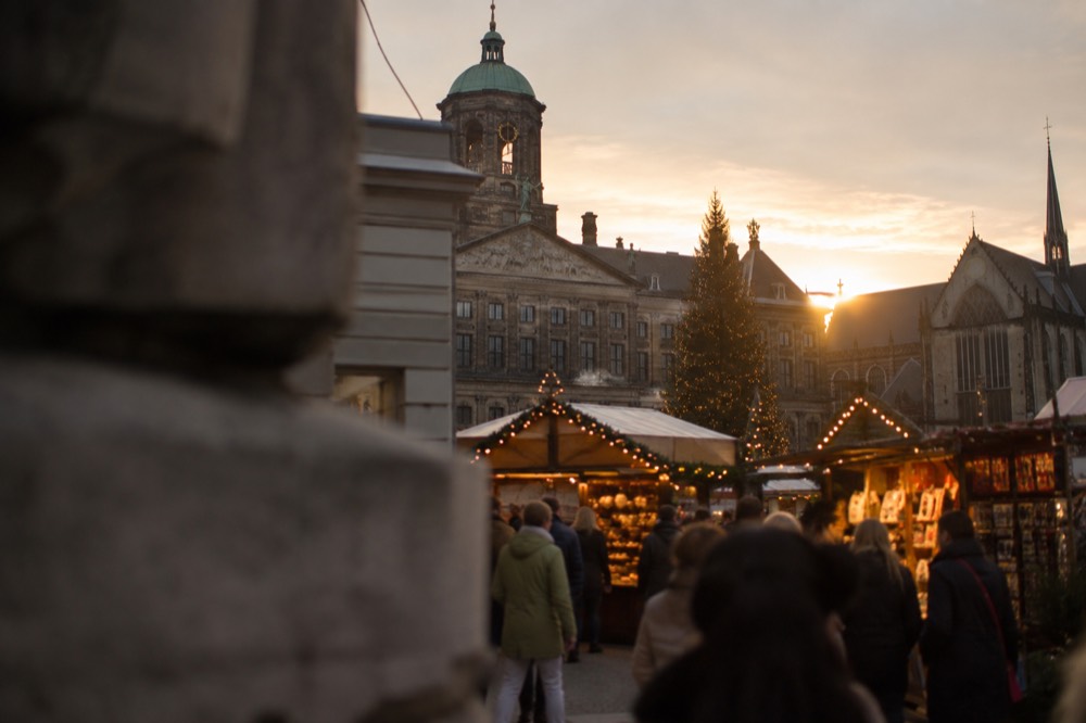 A Christmas market stall glowing with warm lights beside historic Amsterdam buildings at dusk