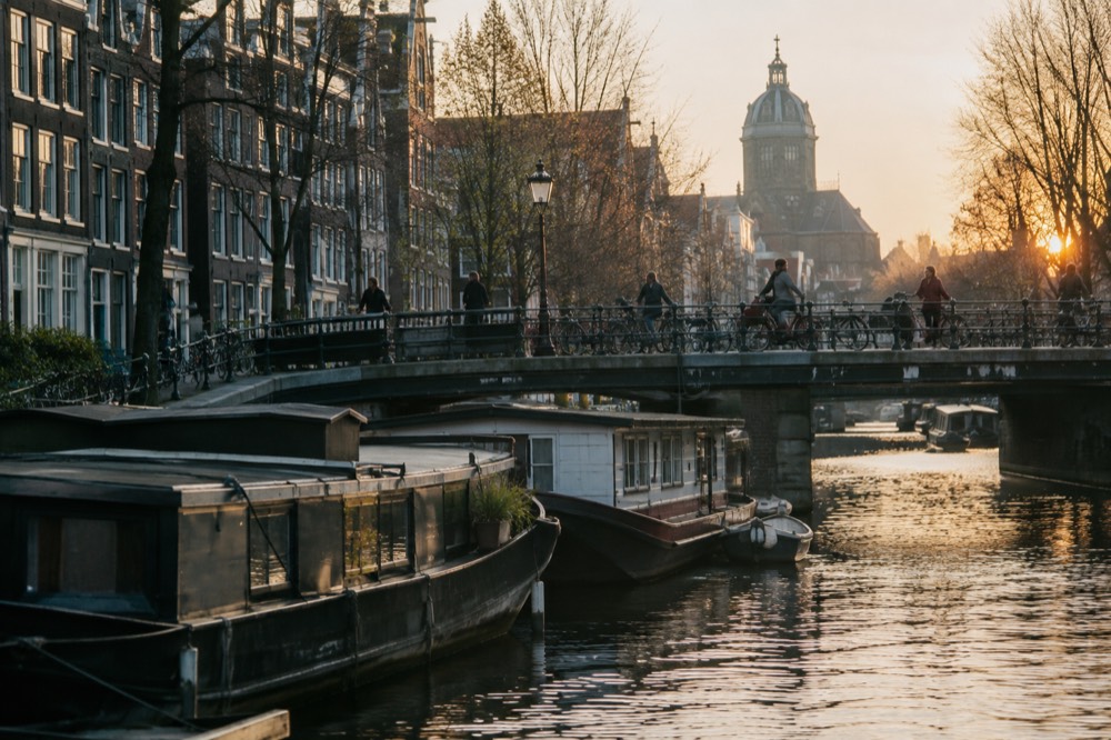 Evening light on a canal bridge with houseboats moored below and bicycles crossing