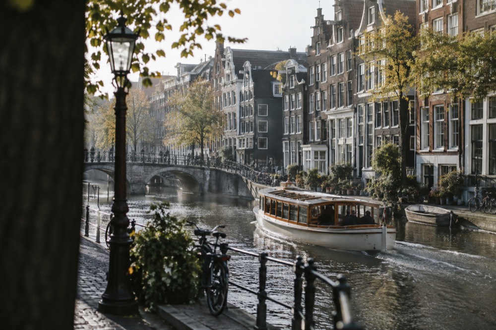 Saloon boat cruising past leaning canal houses on a narrow Amsterdam gracht