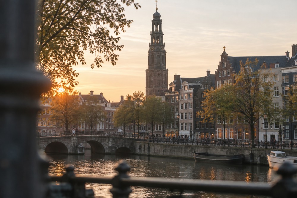 A medieval stone belfry tower rising above gabled rooftops beside a quiet canal