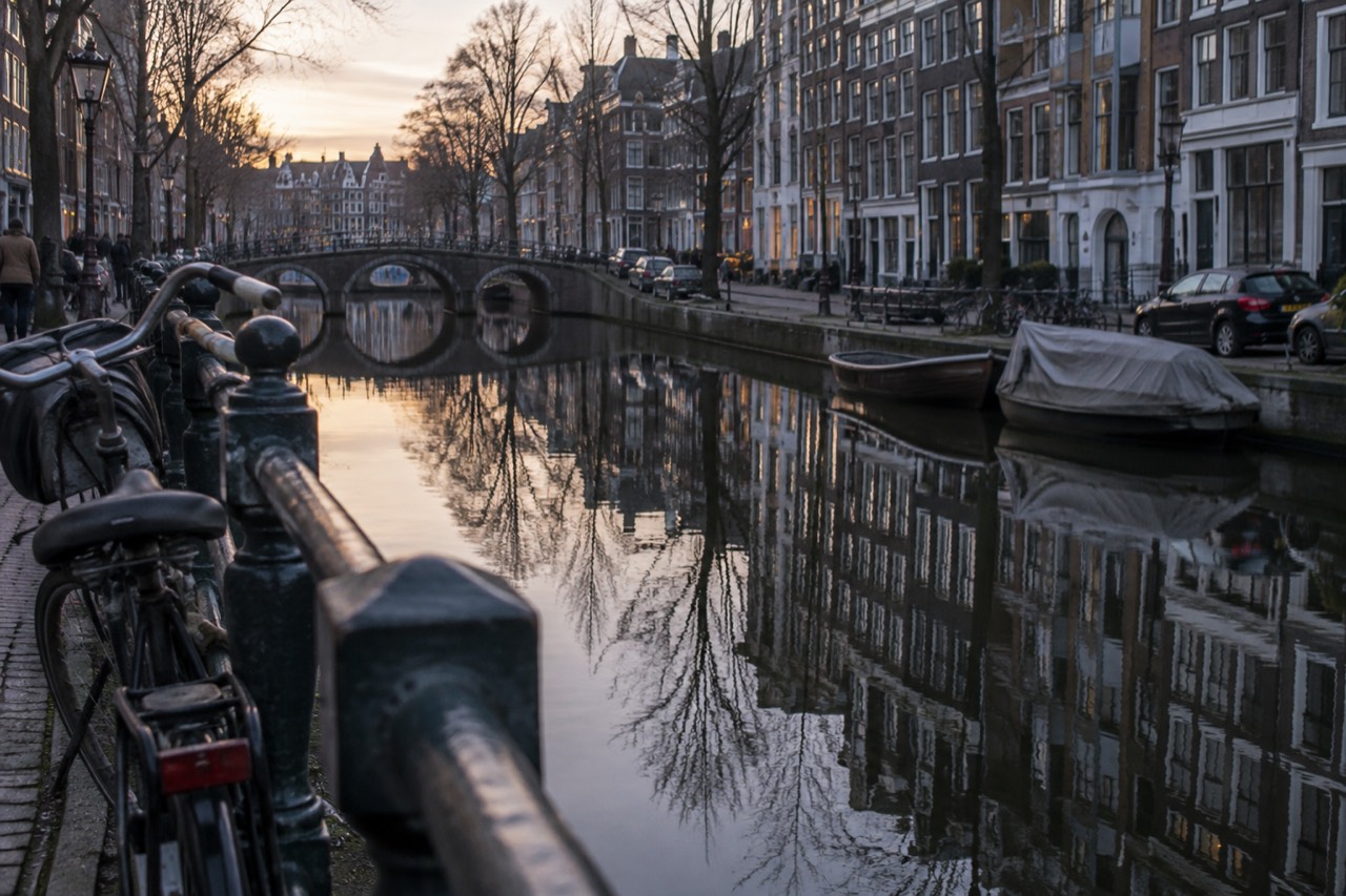 Canal houses reflected in still water along a narrow Amsterdam gracht at dusk