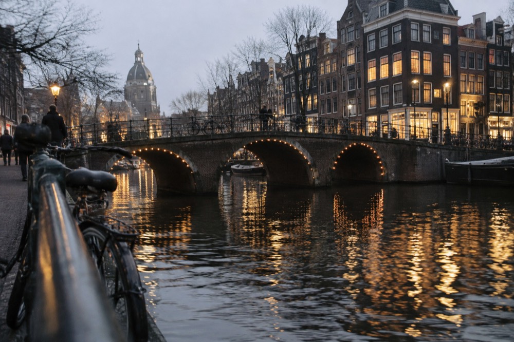 Illuminated canal houses and arched bridge reflected in dark evening water