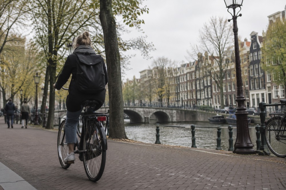 A cyclist riding along a tree-lined Amsterdam bike lane with canal houses in the background