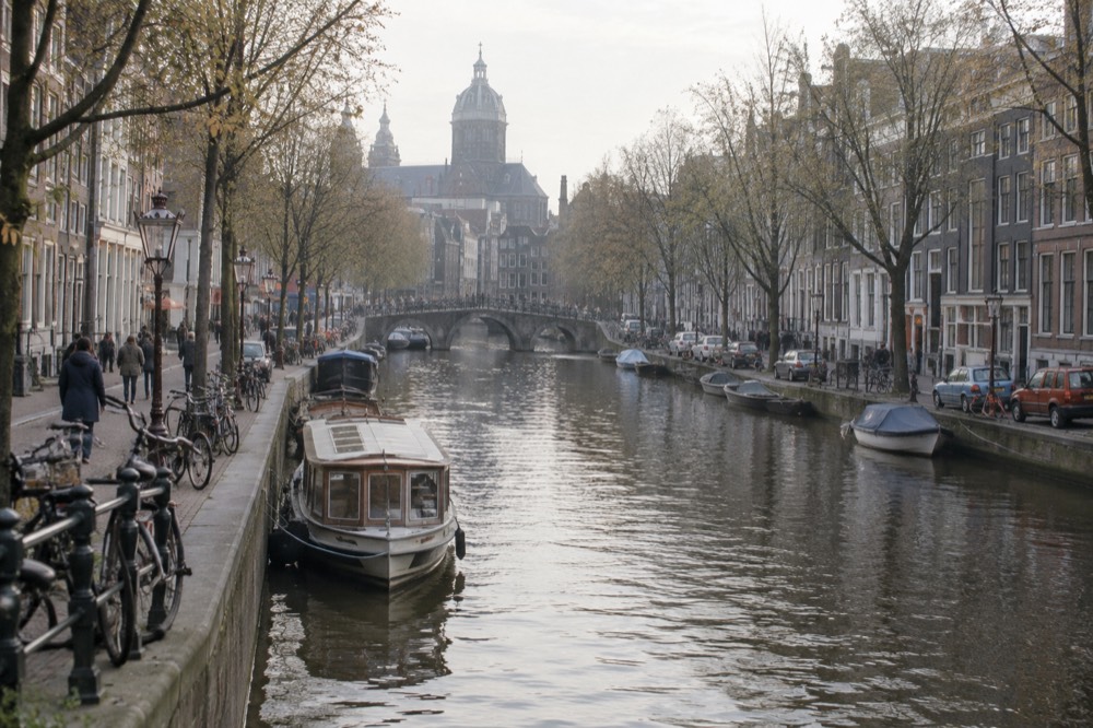 A quiet Amsterdam canal street with parked bicycles along the railings