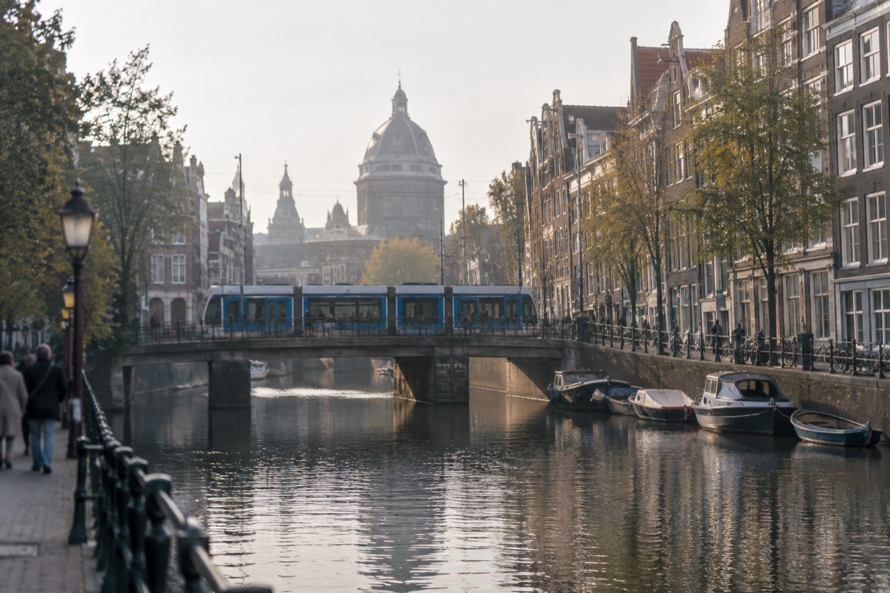 A blue Amsterdam tram crossing a bridge over a canal lined with gabled houses
