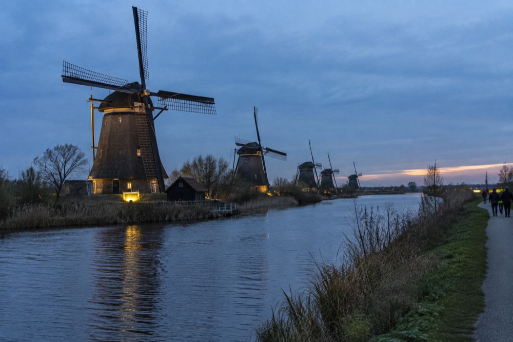 Row of historic Dutch windmills beside a river with a footpath