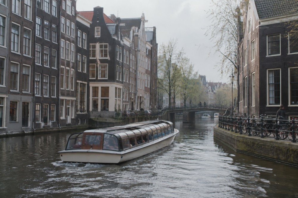A canal cruise boat passing tall gabled houses on a narrow Amsterdam canal
