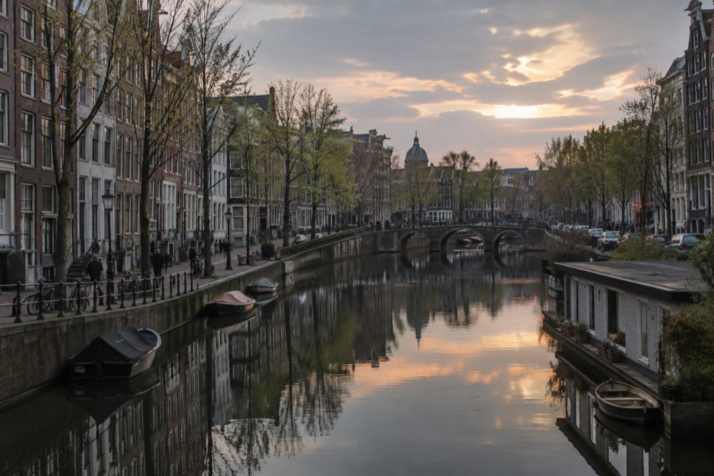 An Amsterdam canal at dusk with brick houses reflected in still water