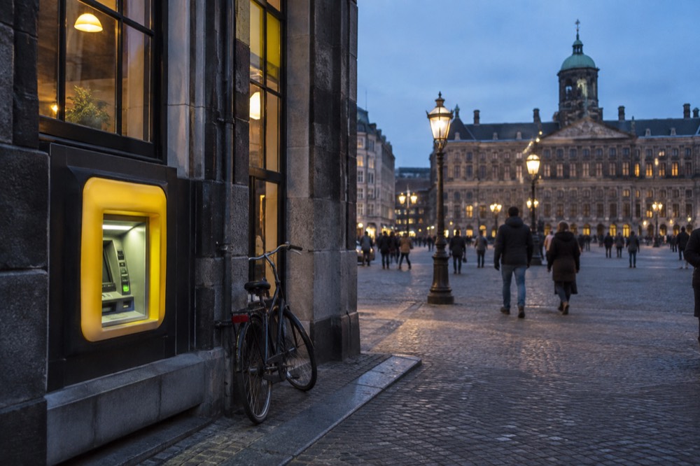 A Geldmaat ATM standing outside a traditional Amsterdam canal house with a bicycle leaning against the wall