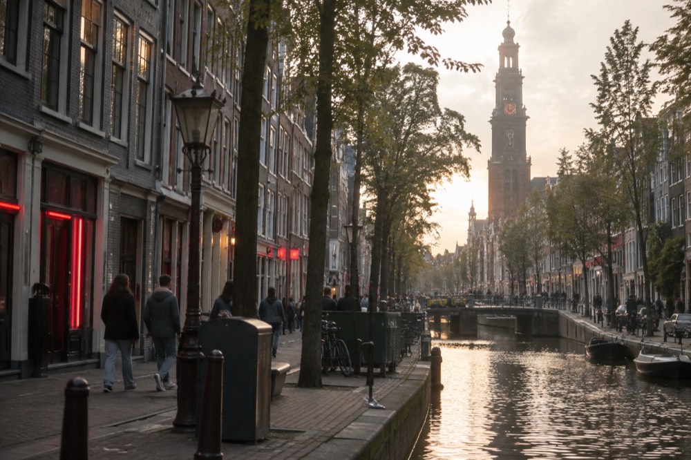 Historic church tower rising above old Amsterdam rooftops in soft evening light