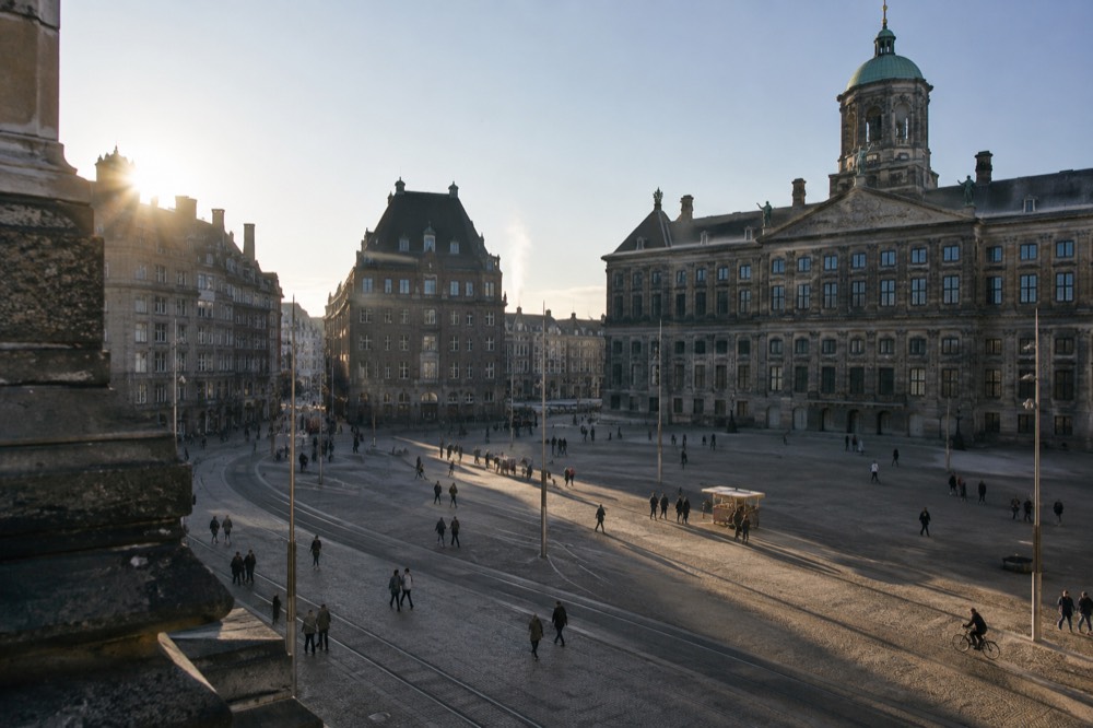 A busy square in central Amsterdam with tram tracks and historic facades