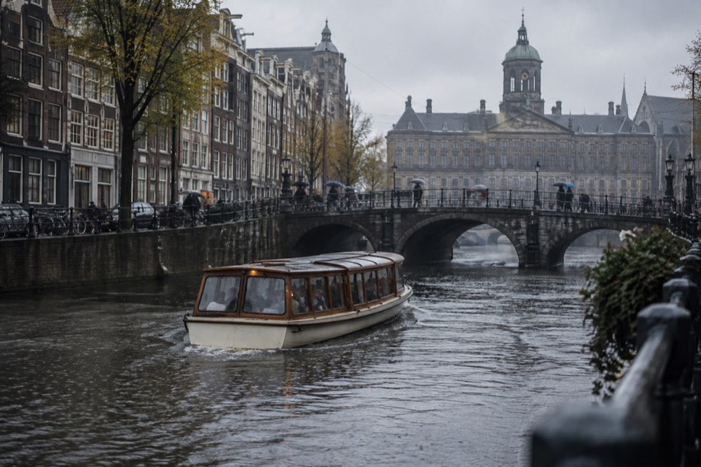 Covered saloon boat cruising along an Amsterdam canal in soft rain