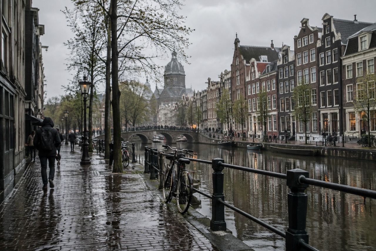 Rainy canal street in Amsterdam with wet cobblestones and gabled houses reflected in the water