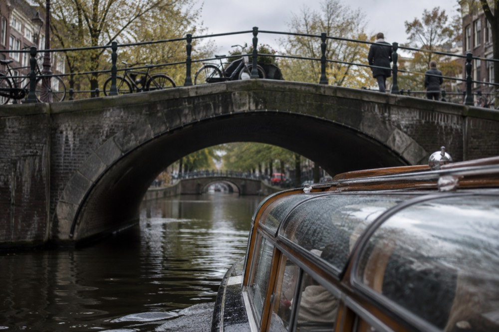 A low canal boat passing under a stone bridge in the canal belt