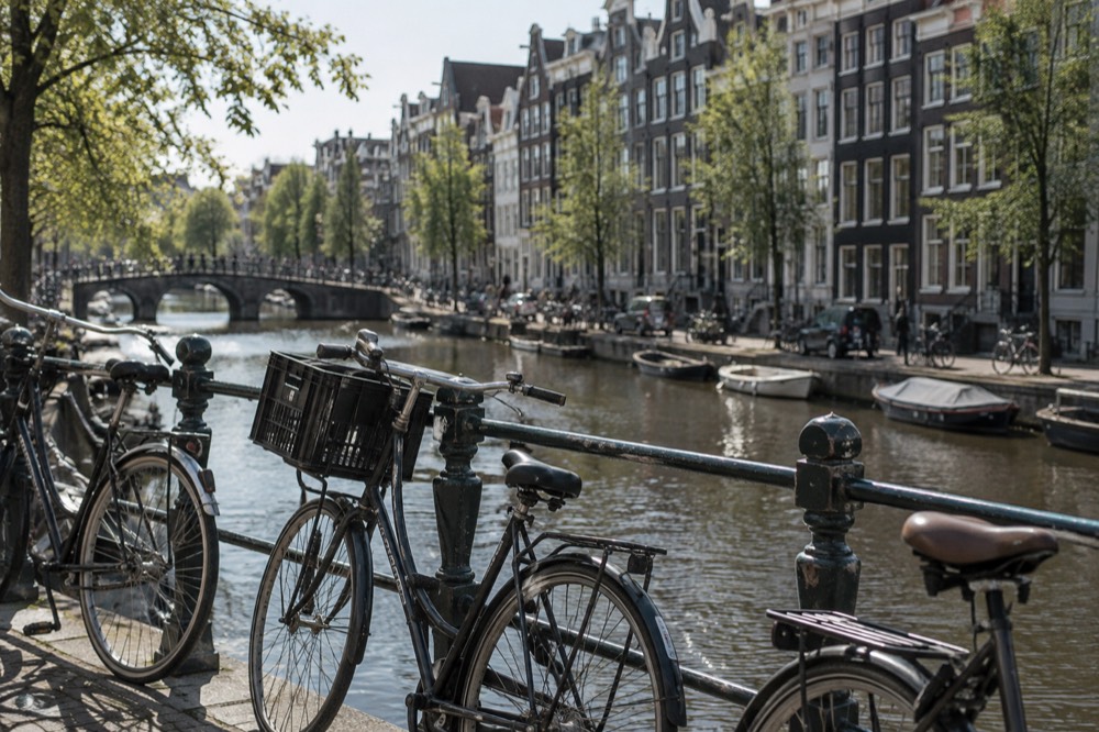 Bicycles chained to a canal railing beside a row of tall narrow gabled houses