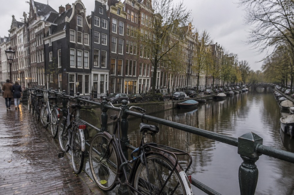 Row of narrow gabled canal houses along a quiet Amsterdam gracht with bicycles chained to a bridge rail