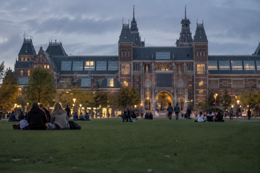 Museumplein with the Rijksmuseum facade and visitors on the lawn in late afternoon light
